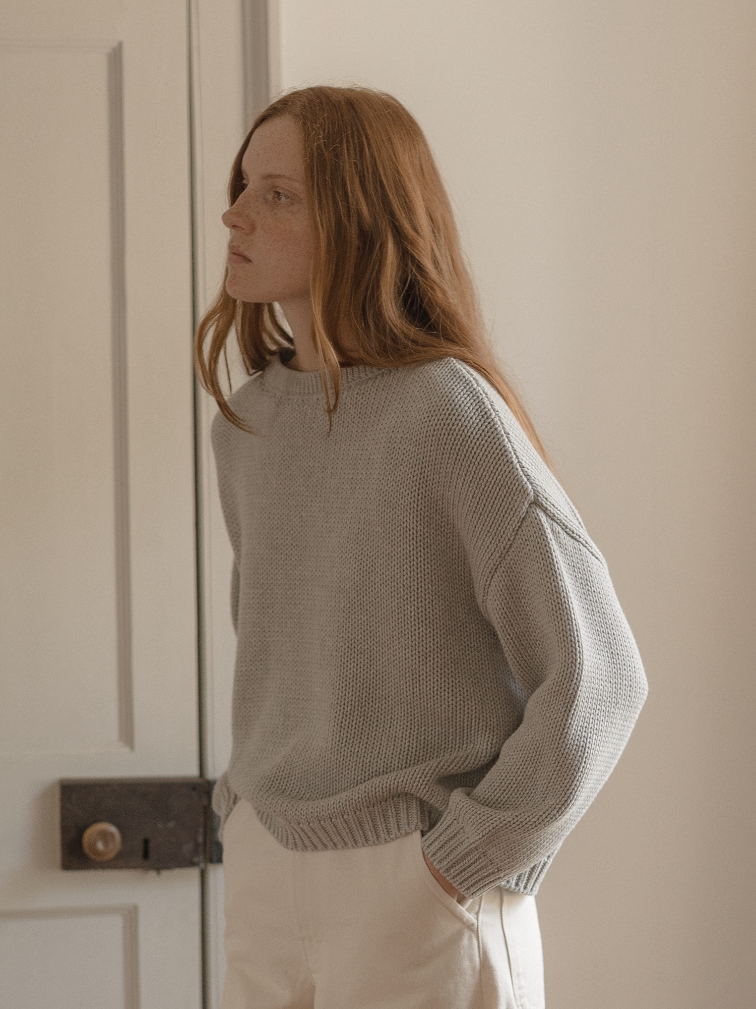 Model wearing the Townes Pullover in Pebble by Gillian Stevens, three-quarter back view beside a door