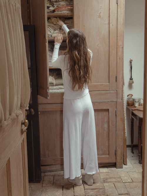 Model wearing the Calla Pant in Salt by Gillian Stevens, back view at a rustic wooden armoire