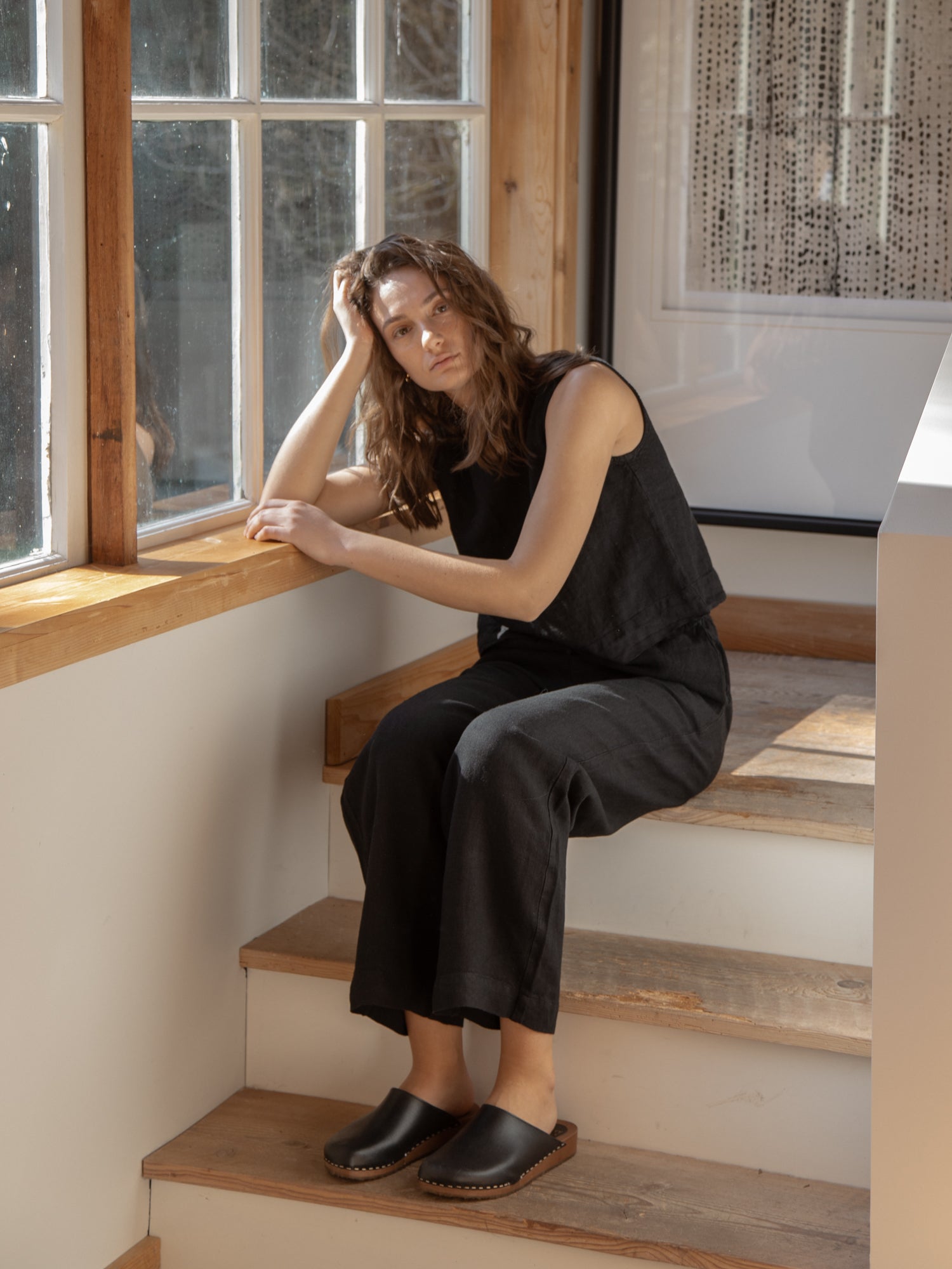 Model wearing the Finley Top in Noir by Gillian Stevens, seated on stairs by a window