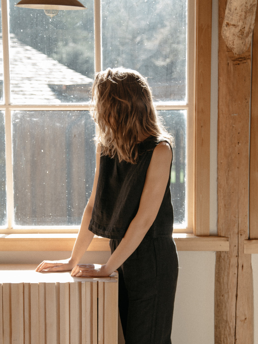 Model wearing the Finley Top in Noir by Gillian Stevens, back view by a window in a wooden interior