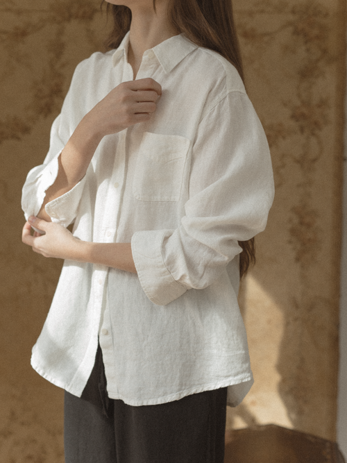 Person wearing a Britta Shirt Linen Salt by Gillian Stevens with rolled-up sleeves against a brown background.