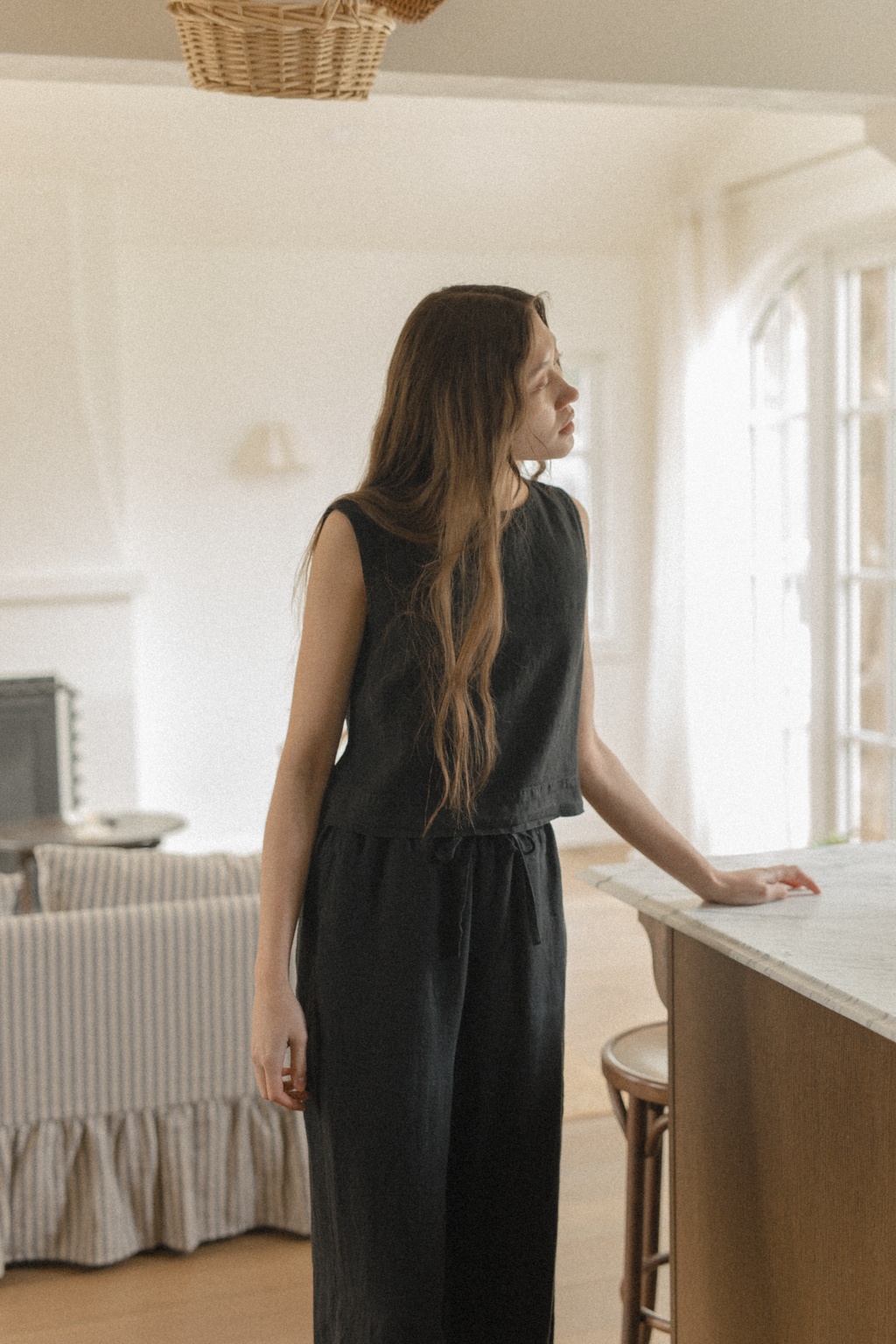 Model wearing the Finley Top in Noir by Gillian Stevens, back view in a styled kitchen setting