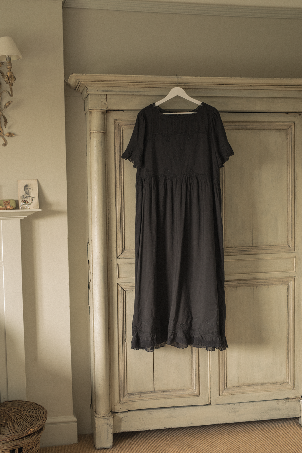 The Astrid Dress in Noir by Gillian Stevens, hung on wardrobe in styled room setting