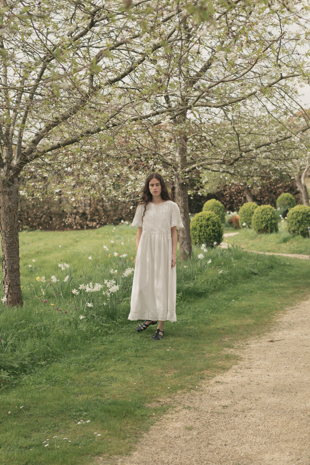 Model wearing the Astrid Dress in Salt by Gillian Stevens, full-length front view in a garden orchard setting