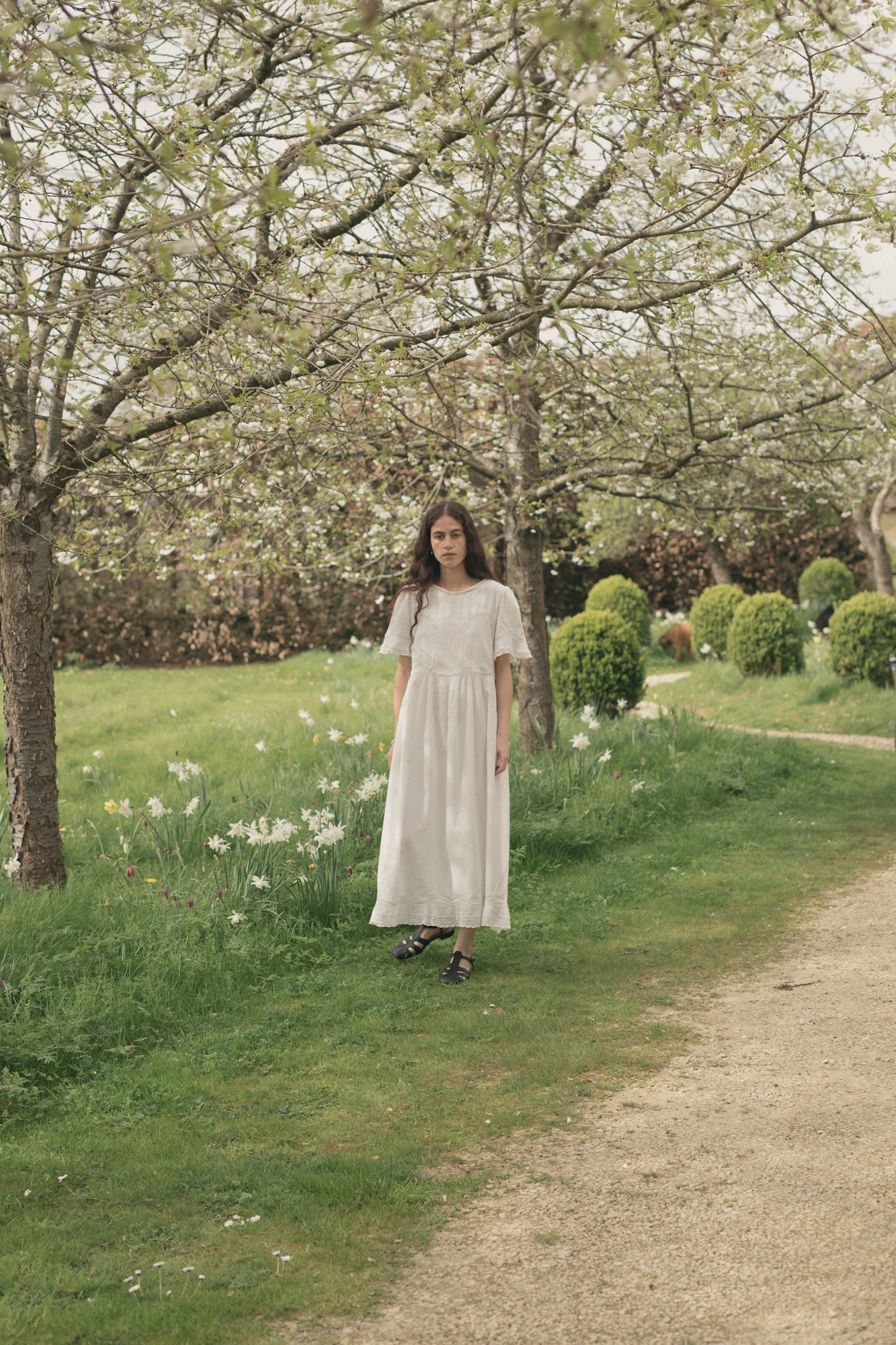 Model wearing the Astrid Dress in Salt by Gillian Stevens, full-length front view in a garden orchard setting