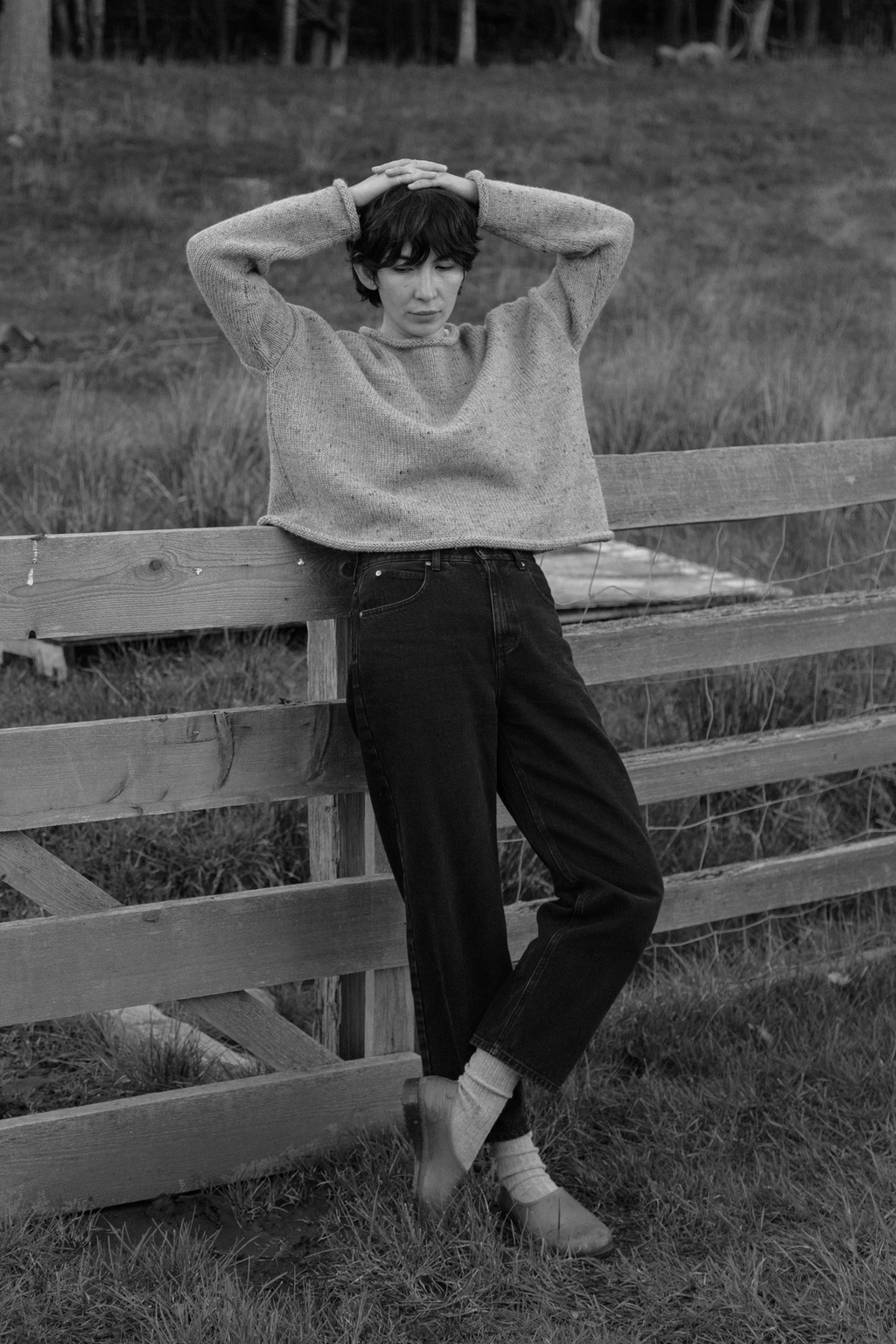 Model wearing the Dara Jean in Noir by Gillian Stevens, leaning against a wooden fence in a rural setting