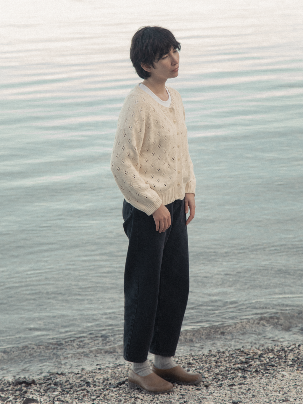 Model wearing the Dara Jean in Noir by Gillian Stevens, side view at a rocky waterside