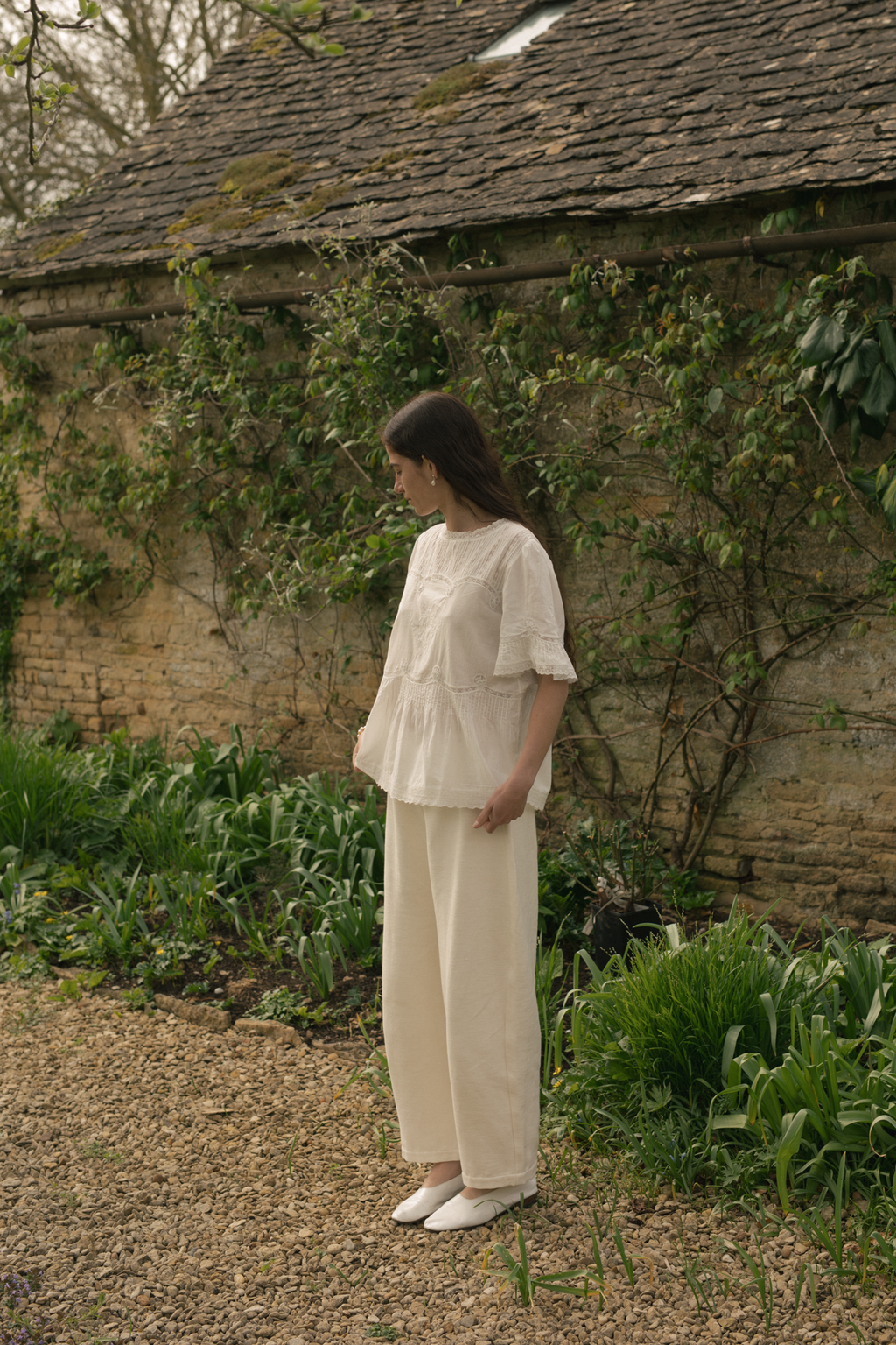 Model wearing the Astrid Blouse in Salt by Gillian Stevens, side view in a garden setting