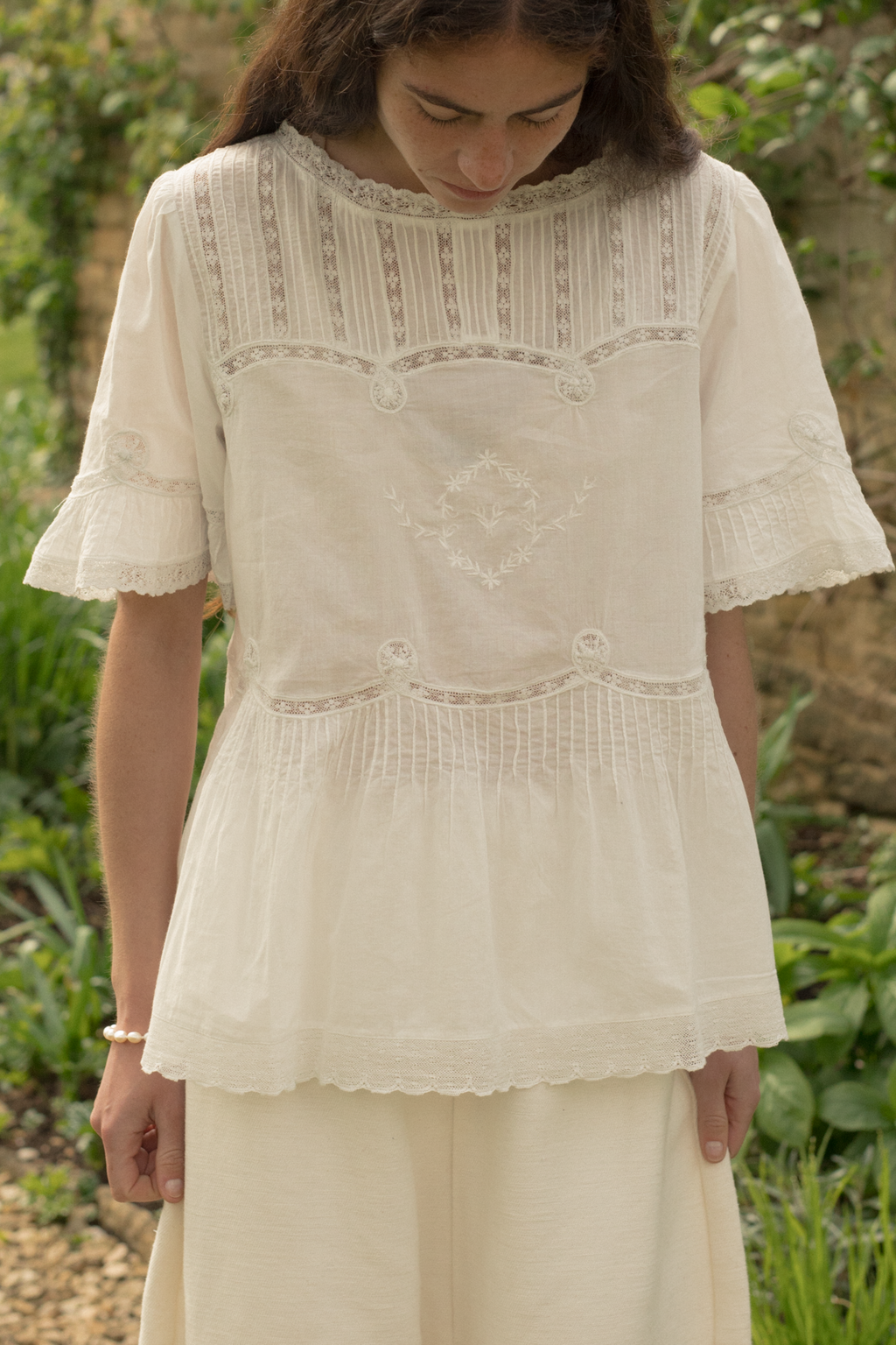 Woman wearing a white embroidered blouse, the Astrid blouse in salt by Gillian Stevens, and pants in a natural setting