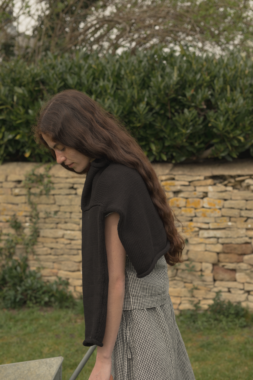 Model wearing the Lennon Cardigan in Noir by Gillian Stevens, side profile in outdoor garden setting