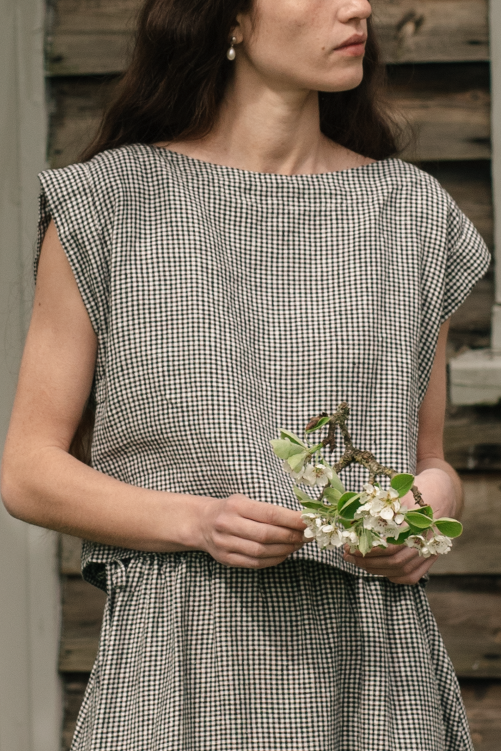 Model wearing the Valley Top in Gingham Noir by Gillian Stevens, front view holding spring blossoms