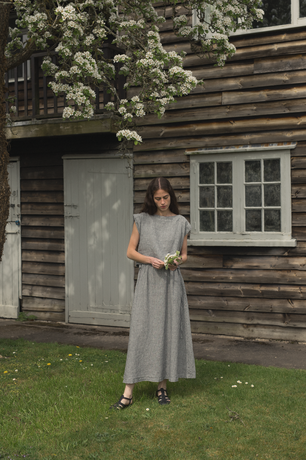 Model wearing the Valley Top in Gingham Noir by Gillian Stevens, full-length outdoor setting with blossom tree