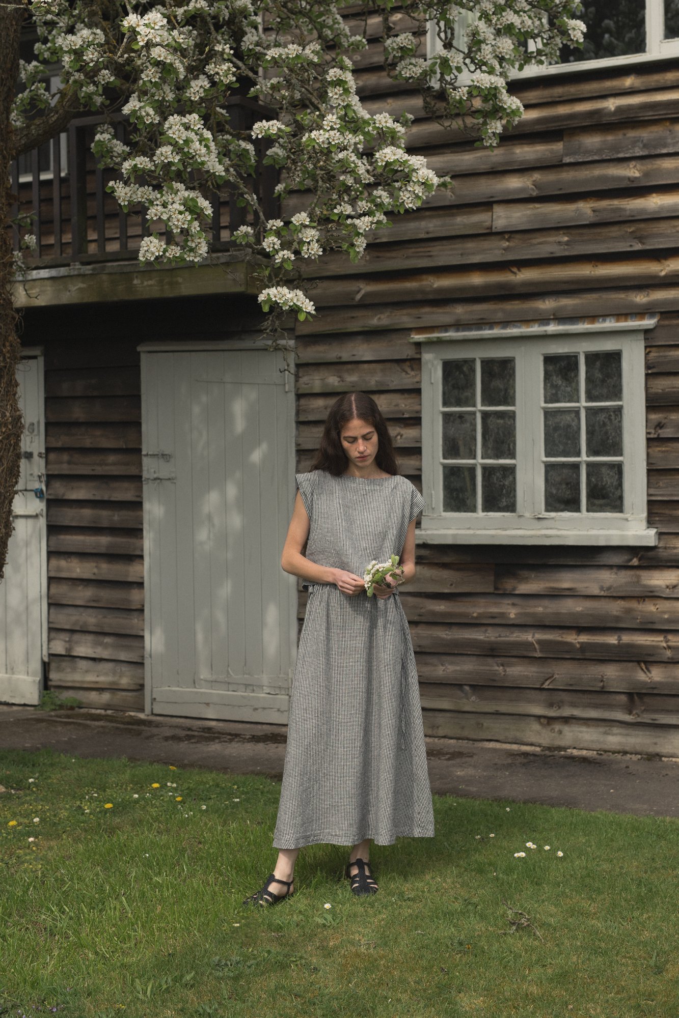 Model wearing the Valley Top in Gingham Noir by Gillian Stevens, full-length outdoor setting with blossom tree