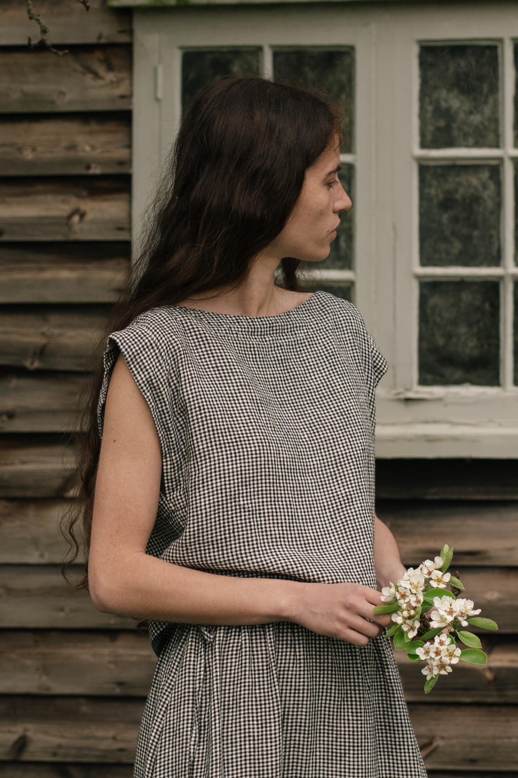 Model wearing the Valley Top in Gingham Noir by Gillian Stevens, side profile holding spring blossoms