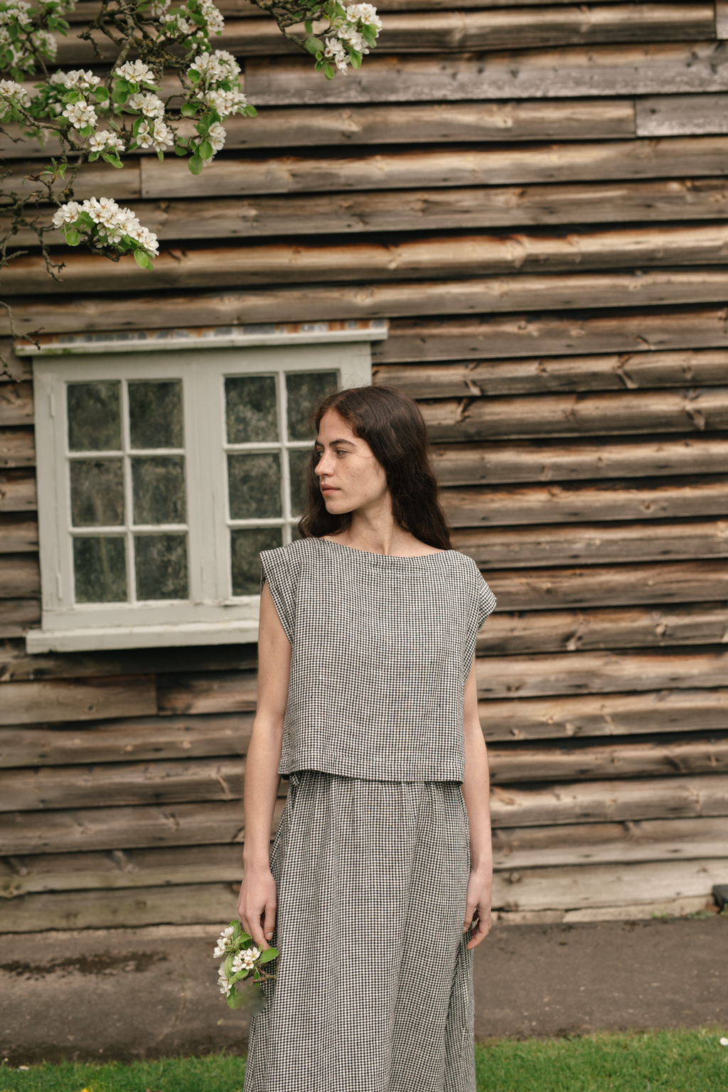 Model wearing the Valley Top in Gingham Noir by Gillian Stevens, front view outdoors by rustic wooden wall