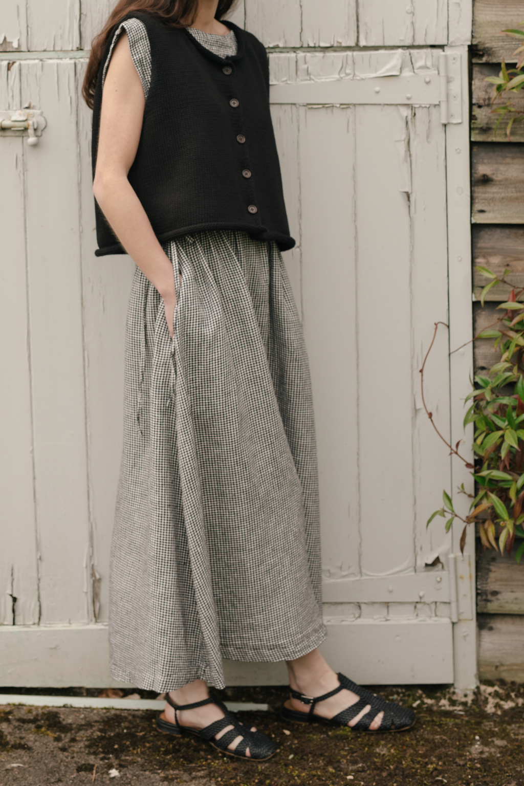 Model wearing the Frances Skirt in Gingham Noir by Gillian Stevens, side view styled with black knit vest outdoors
