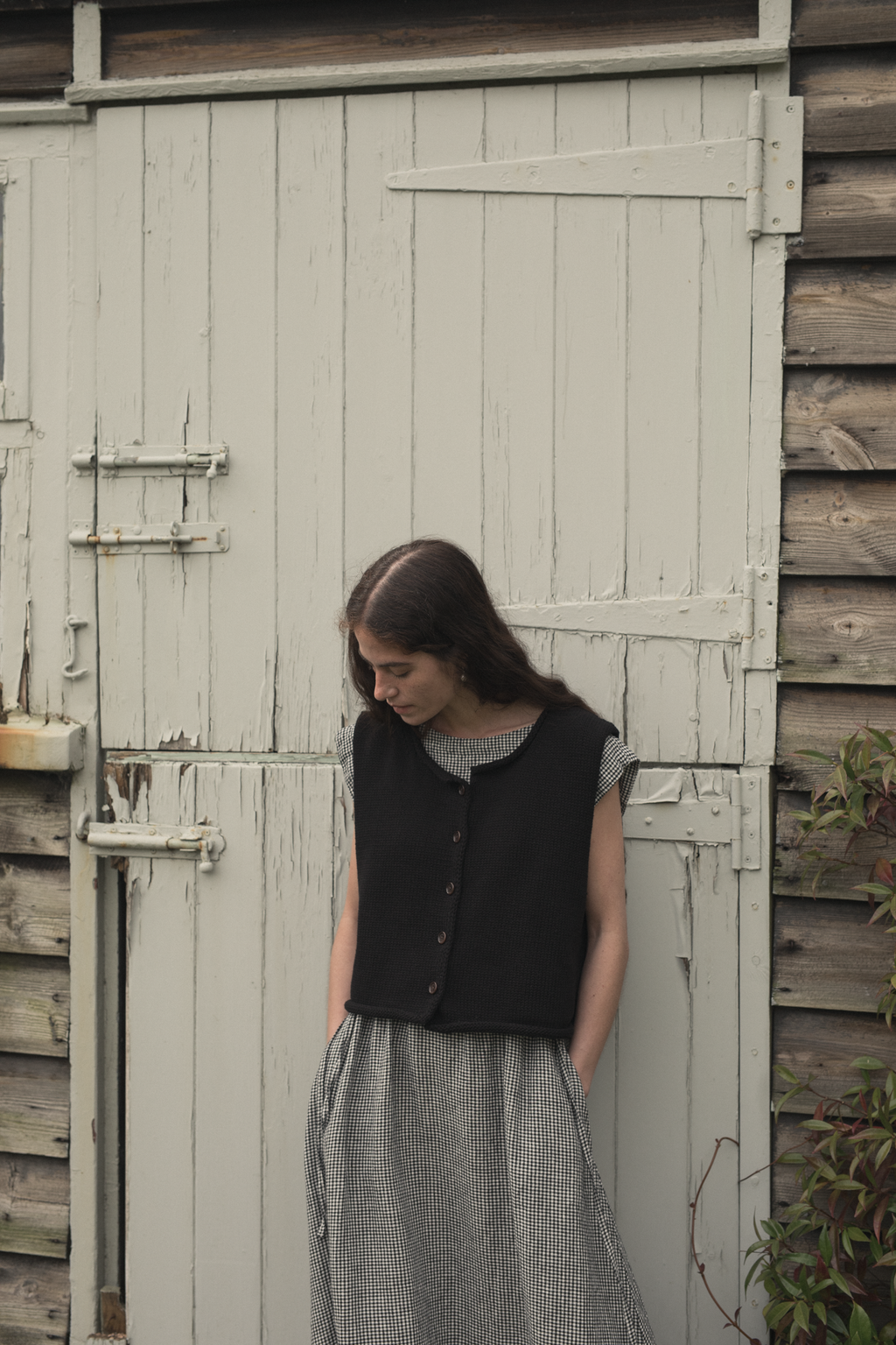 Model wearing the Lennon Vest in Noir by Gillian Stevens, front view against rustic wooden door