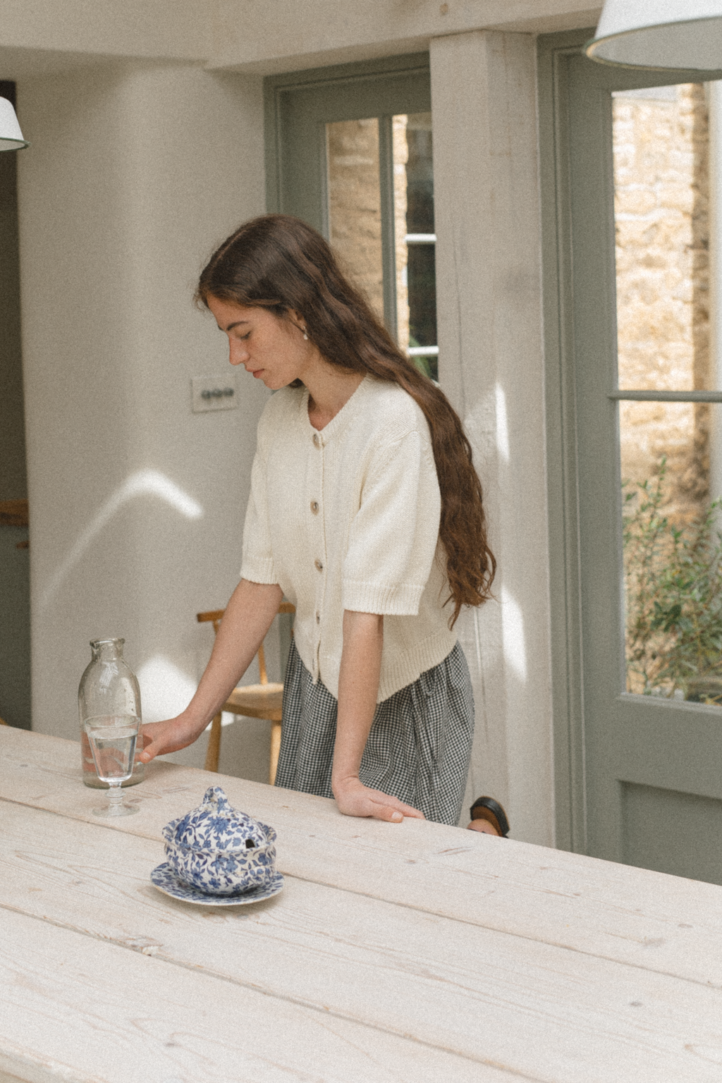 Model wearing the Rosemary Cardigan in Alabaster by Gillian Stevens, side view in a kitchen setting