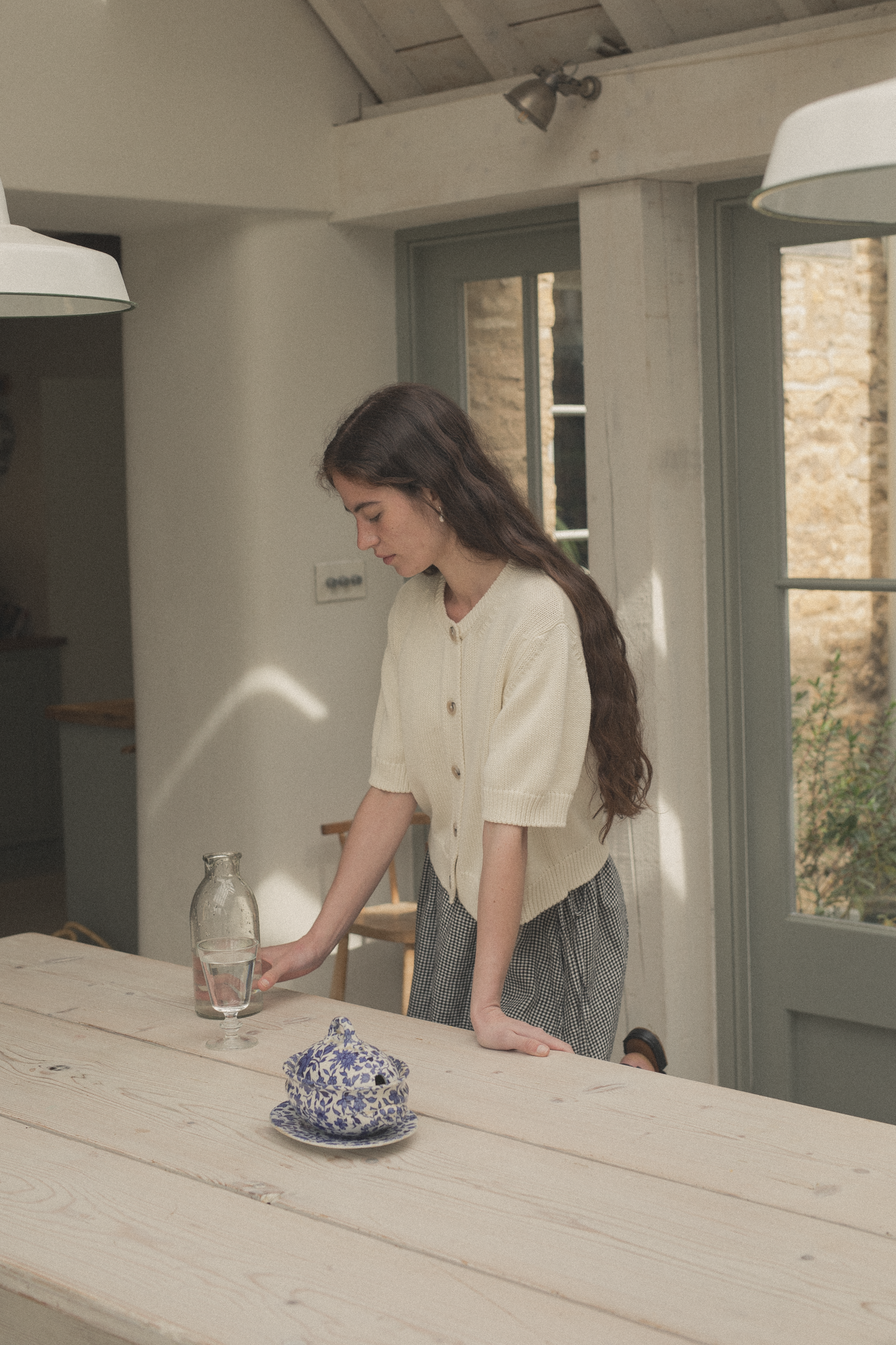 Model wearing the Rosemary Cardigan in Alabaster by Gillian Stevens, side view in kitchen setting