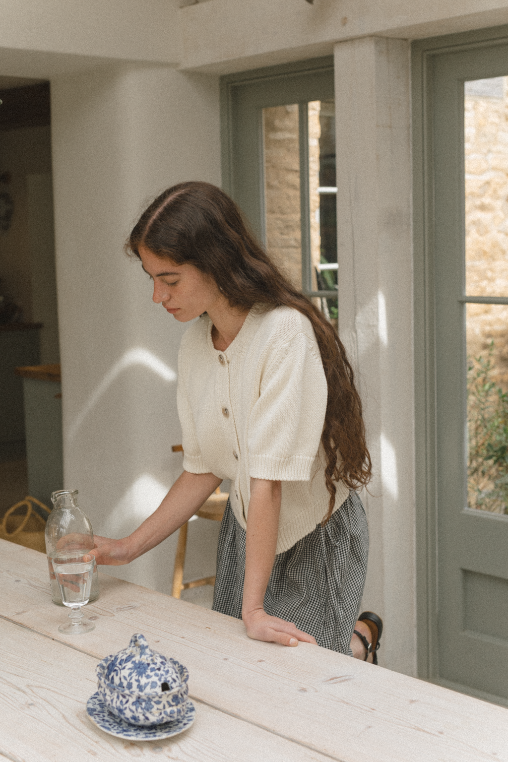 Model wearing the Rosemary Cardigan in Alabaster by Gillian Stevens, side view in a sunlit interior setting