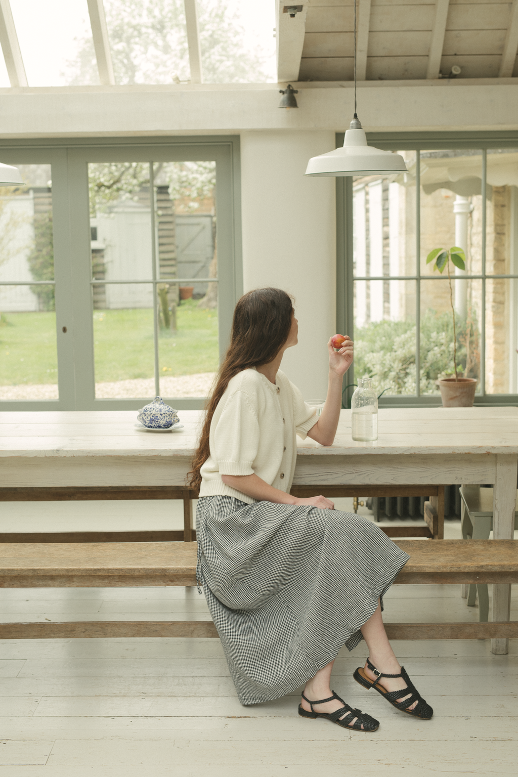 Model wearing the Frances Skirt in Gingham Noir by Gillian Stevens, side view seated in a conservatory