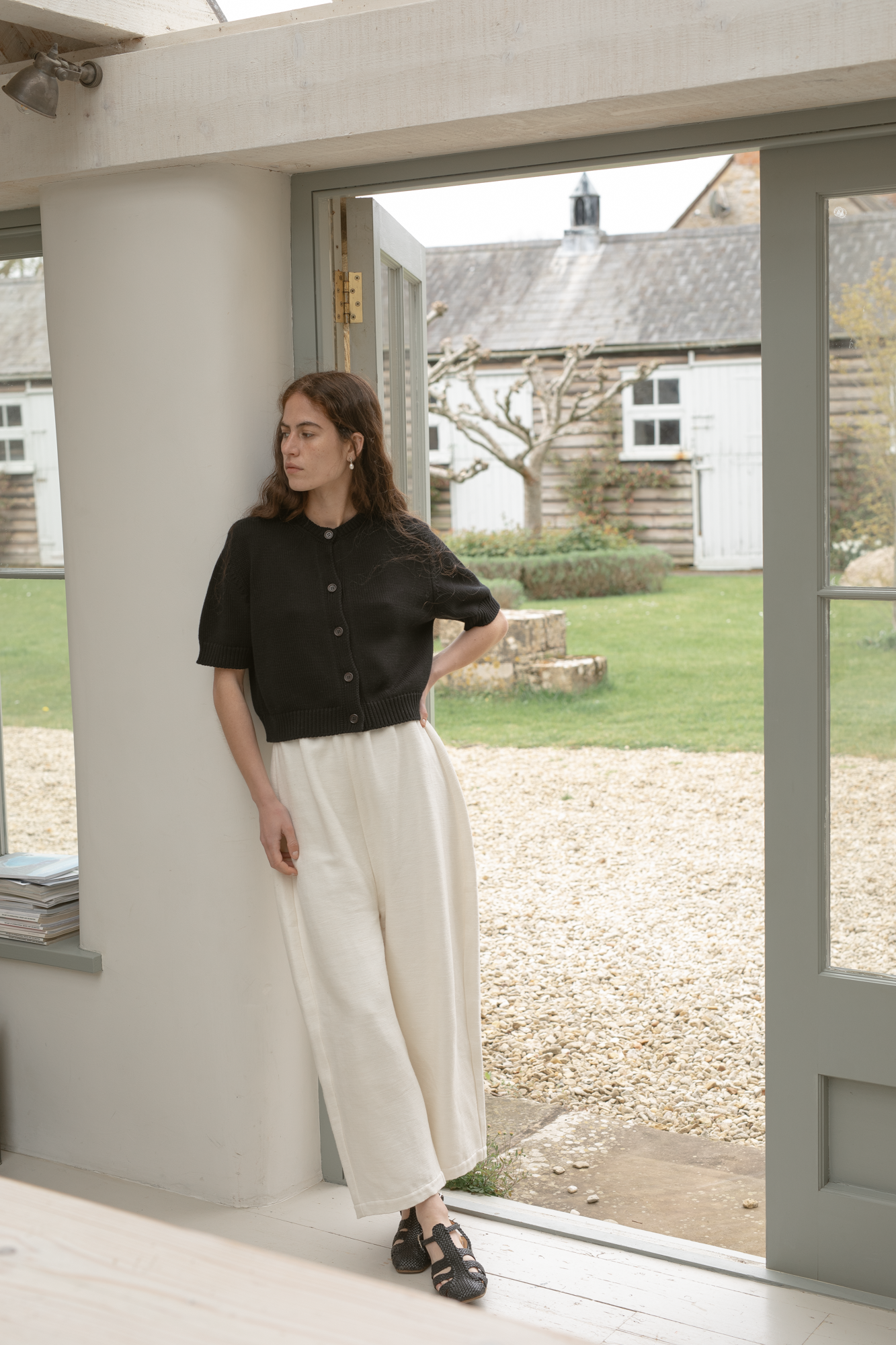 Woman standing in a door way with a view of a farm outside wearing the rosemary cardigan in Noir by Gillian Stevens,