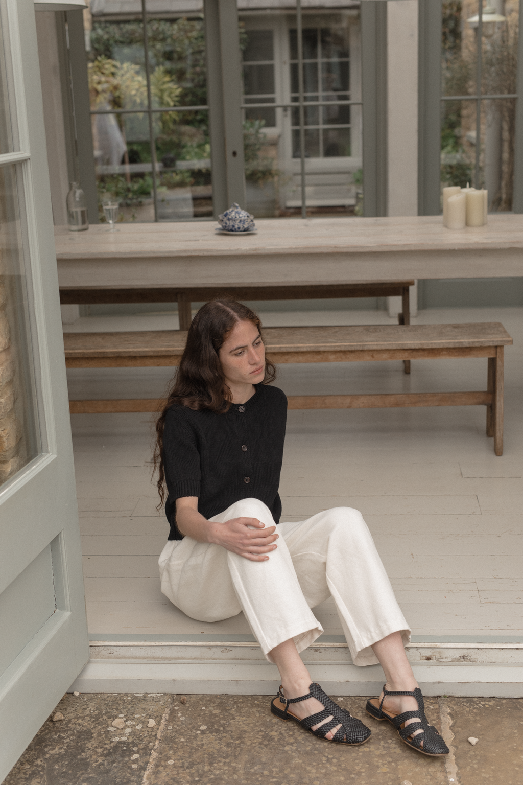 Woman sitting on the ground inside a building with large windows wearing the rosemary cardigan in noir by Gillian Stevens