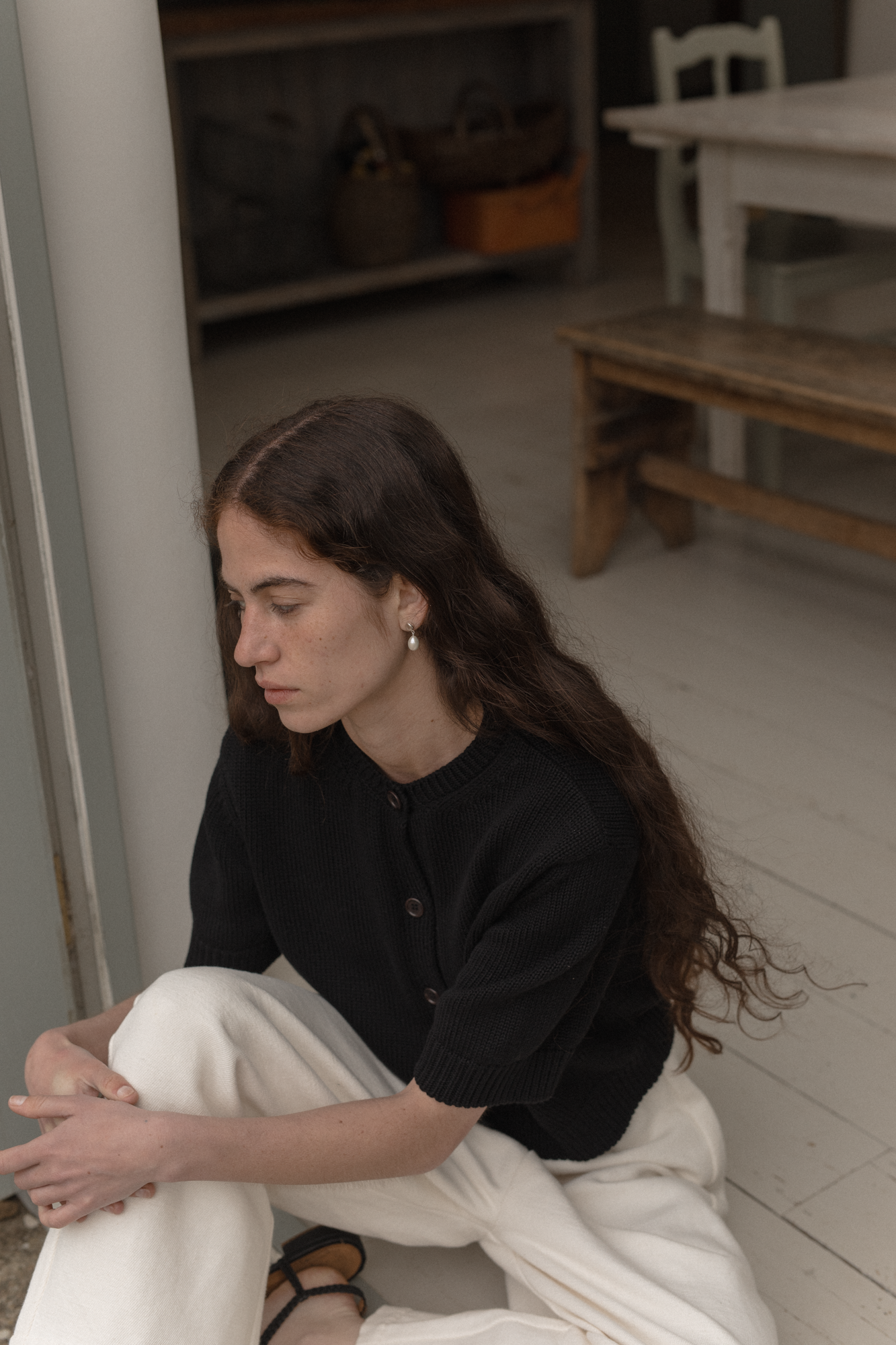 Woman sitting on the floor in a room with wooden furniture wearing the rosemary cardigan in noir by Gillian Stevens