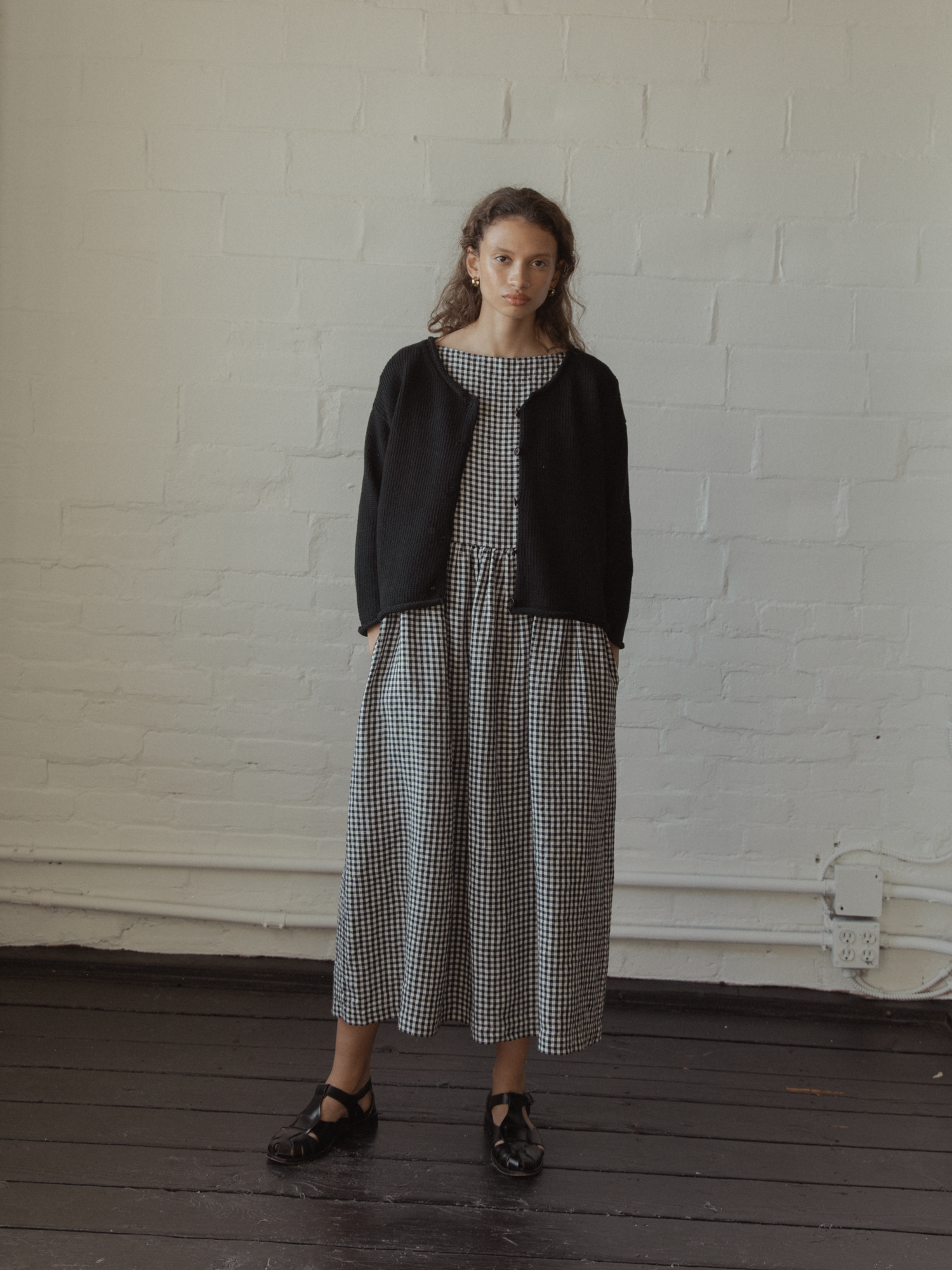 Model wearing the Lennon Cardigan in Noir by Gillian Stevens, full-length front view styled over a gingham dress