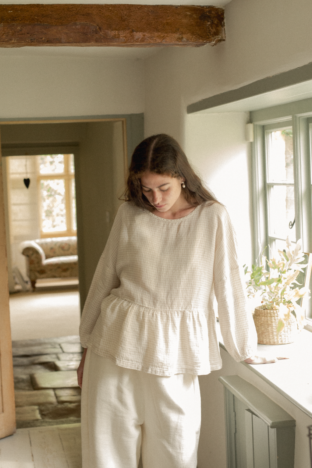 Model wearing the Darla Blouse in Oat Plaid by Gillian Stevens, front view in a rustic interior setting