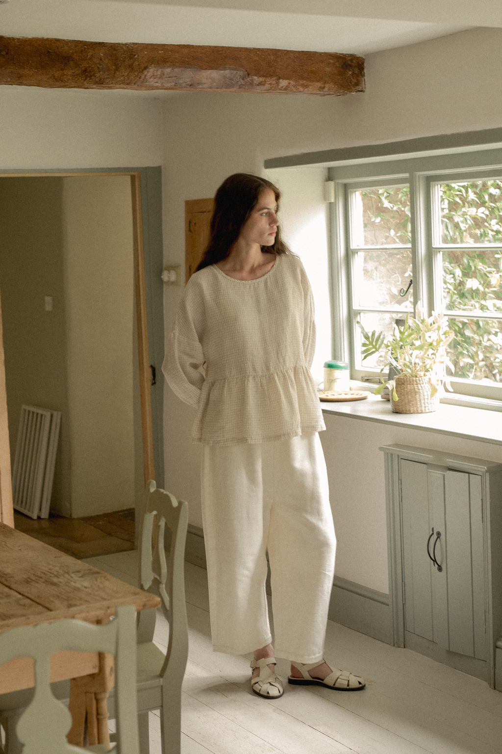 Model wearing the Darla Blouse in Oat Plaid by Gillian Stevens, full-length front view in a cottage kitchen setting