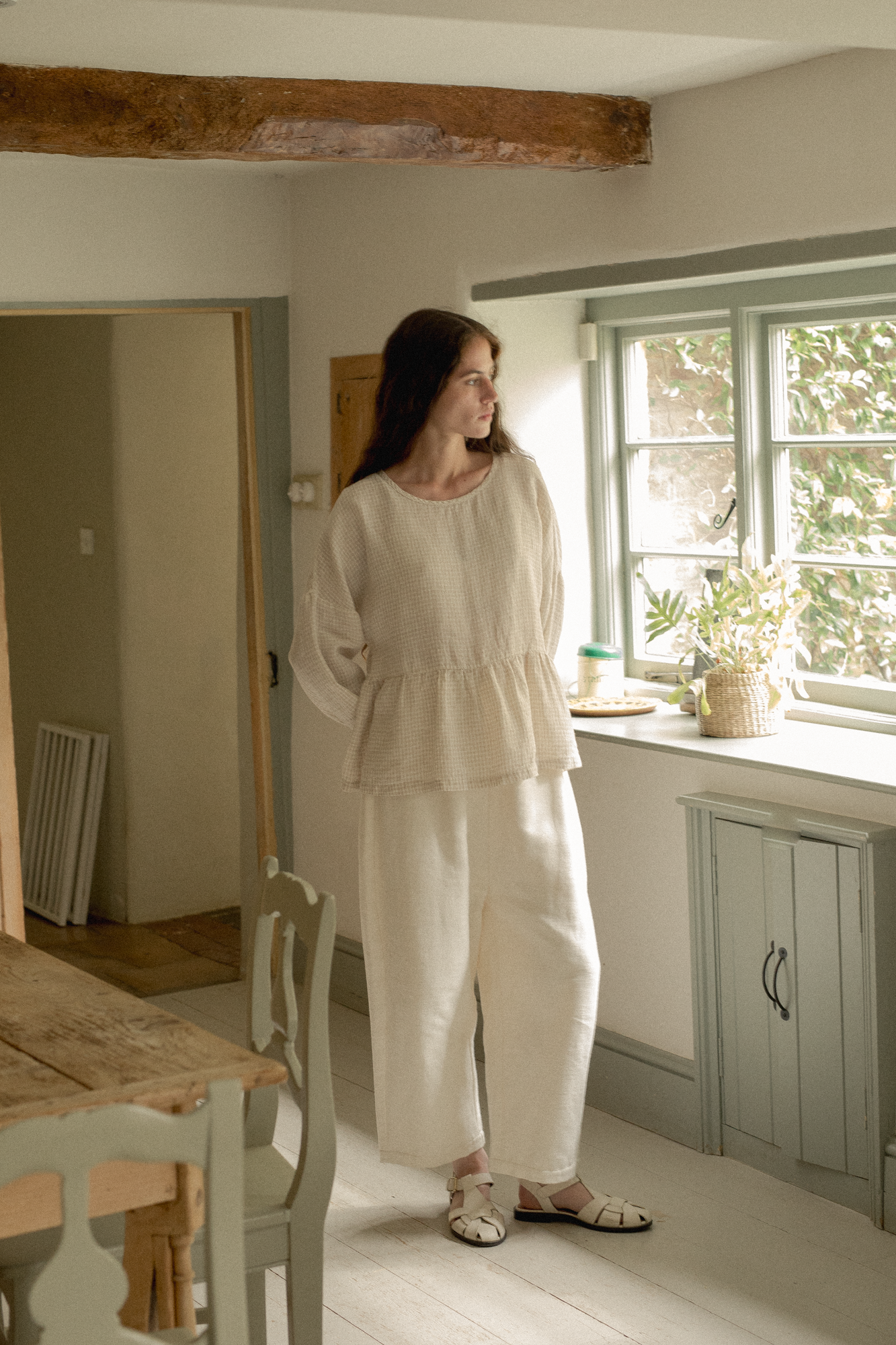 Model wearing the Darla Blouse in Oat Plaid by Gillian Stevens, full-length front view in a cottage kitchen setting