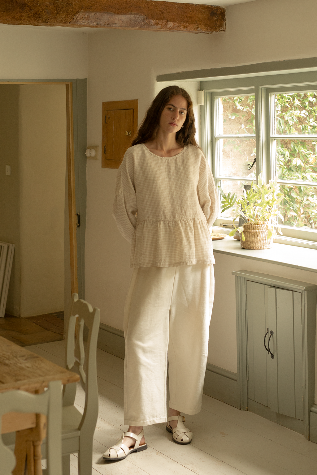 Model wearing the Darla Blouse in Oat Plaid by Gillian Stevens, full-length front view in a cottage kitchen