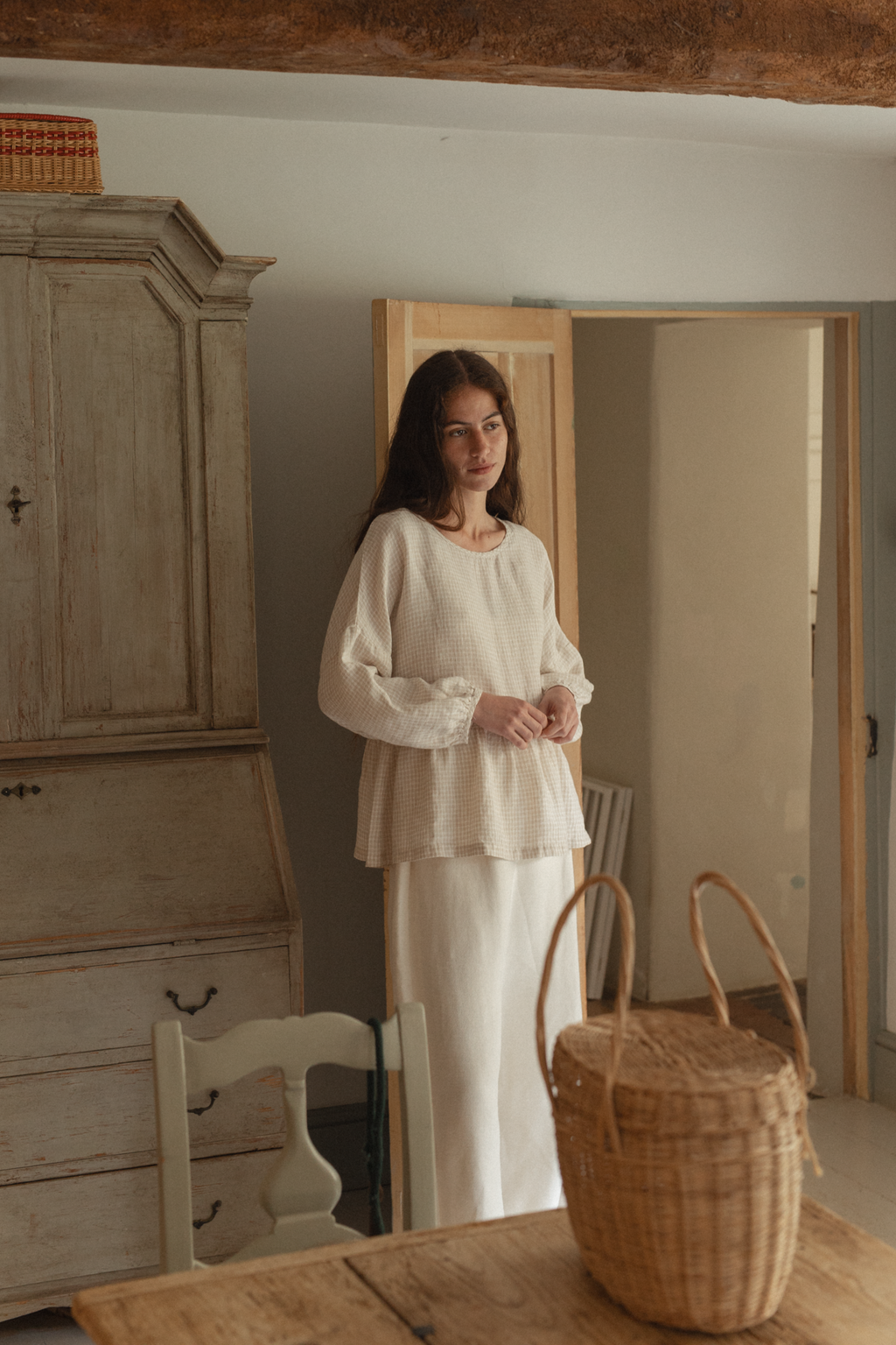 Model wearing the Darla Blouse in Oat Plaid by Gillian Stevens, front view in rustic interior setting