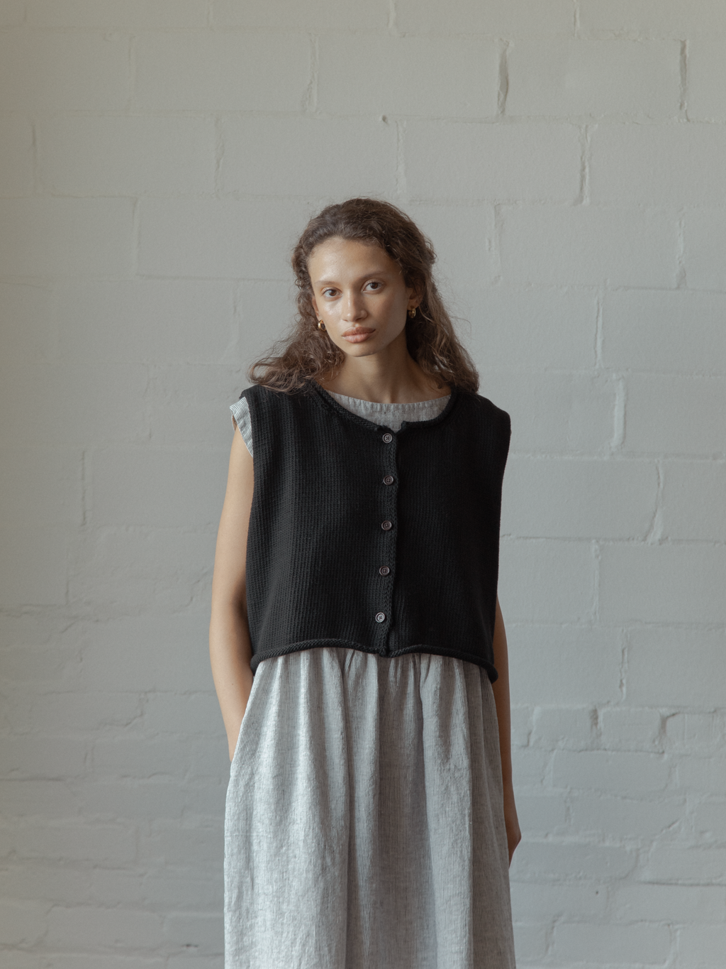 Model wearing the Lennon Vest in Noir by Gillian Stevens, front view showing button detail over striped dress