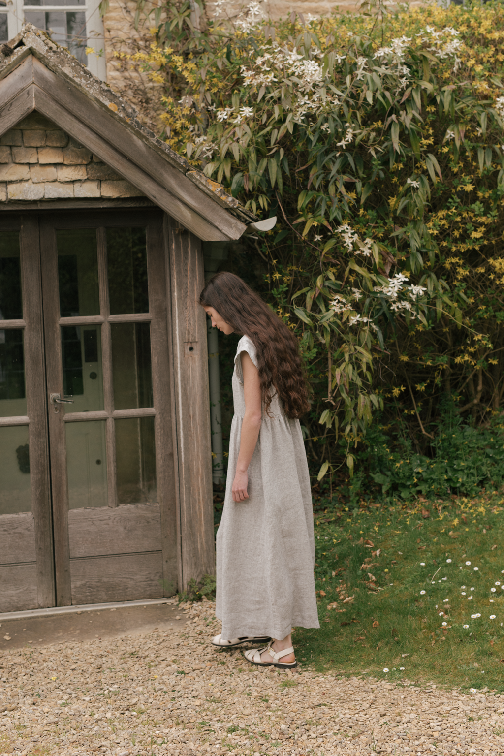 Model wearing the Valley Dress in Charcoal Stripe by Gillian Stevens, side view in garden setting, view 2