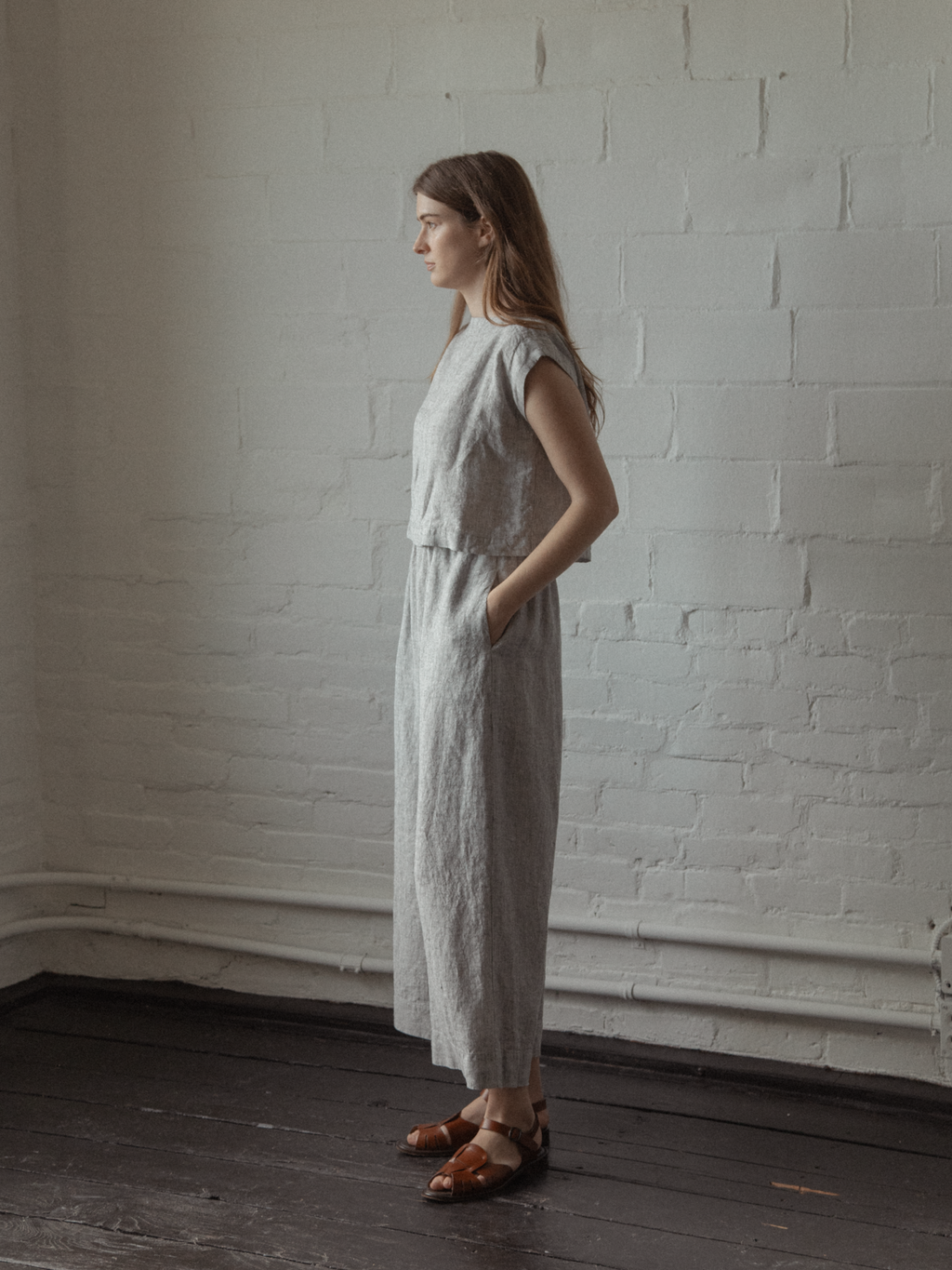 Model wearing the Valley Top in Charcoal Stripe by Gillian Stevens, side view against a white brick wall