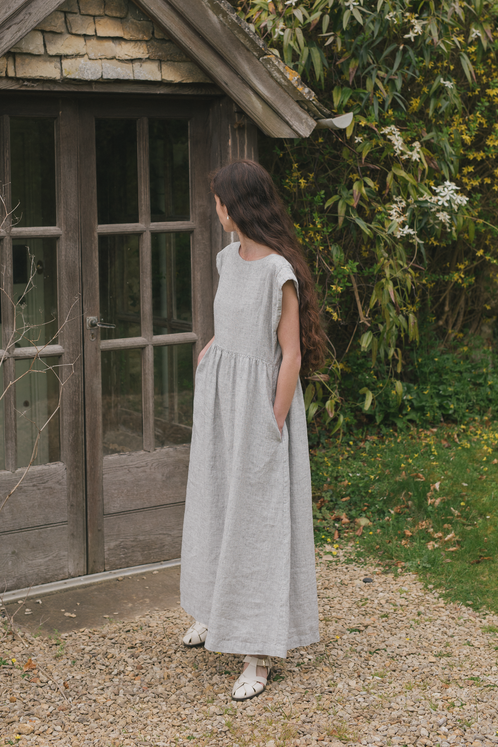 Model wearing the Valley Dress in Charcoal Stripe by Gillian Stevens, side view in garden setting, view 3