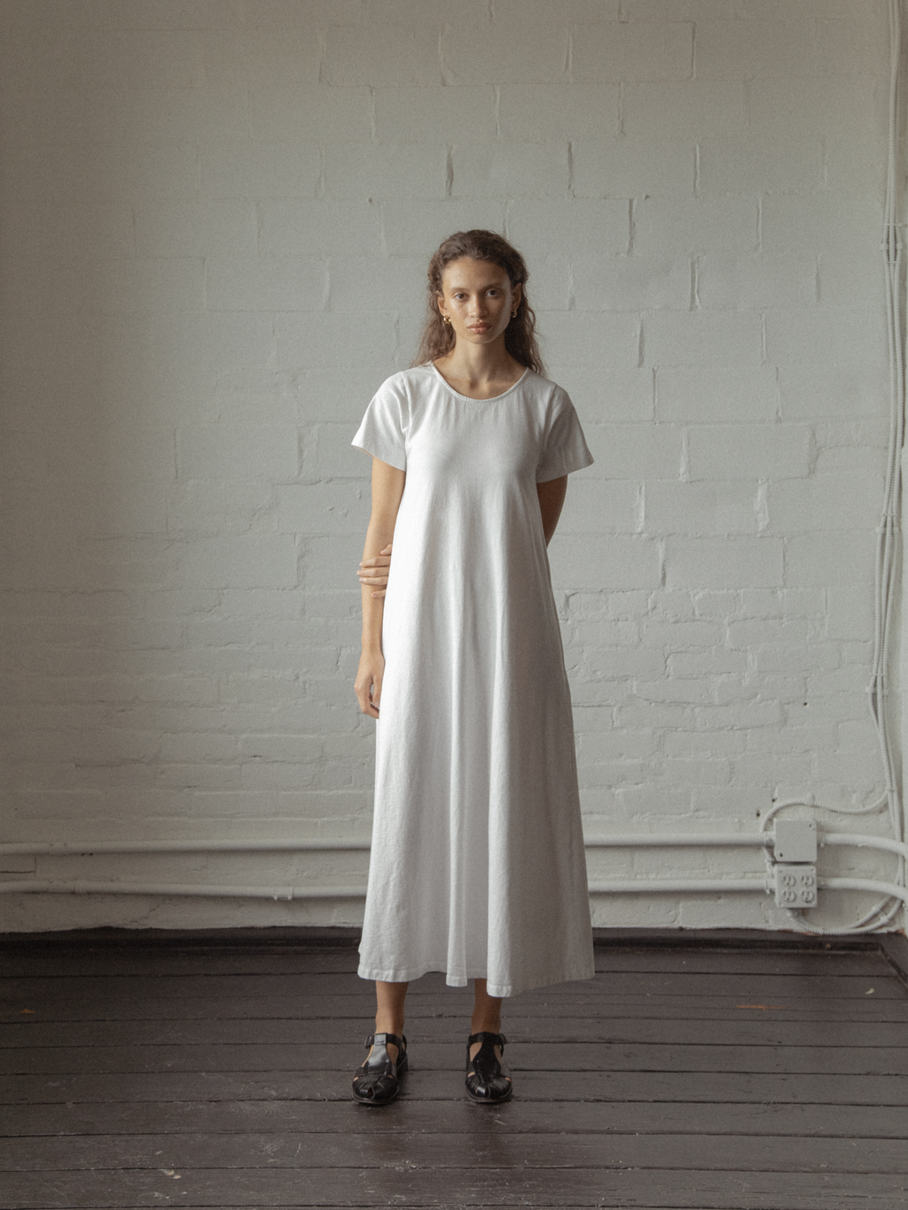Model wearing the Palmer Dress in Salt by Gillian Stevens, front view against a white brick wall