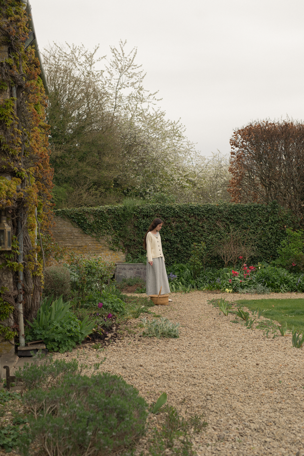 Model wearing the Lennon Cardigan in Ivory by Gillian Stevens, side view in a cottage garden setting