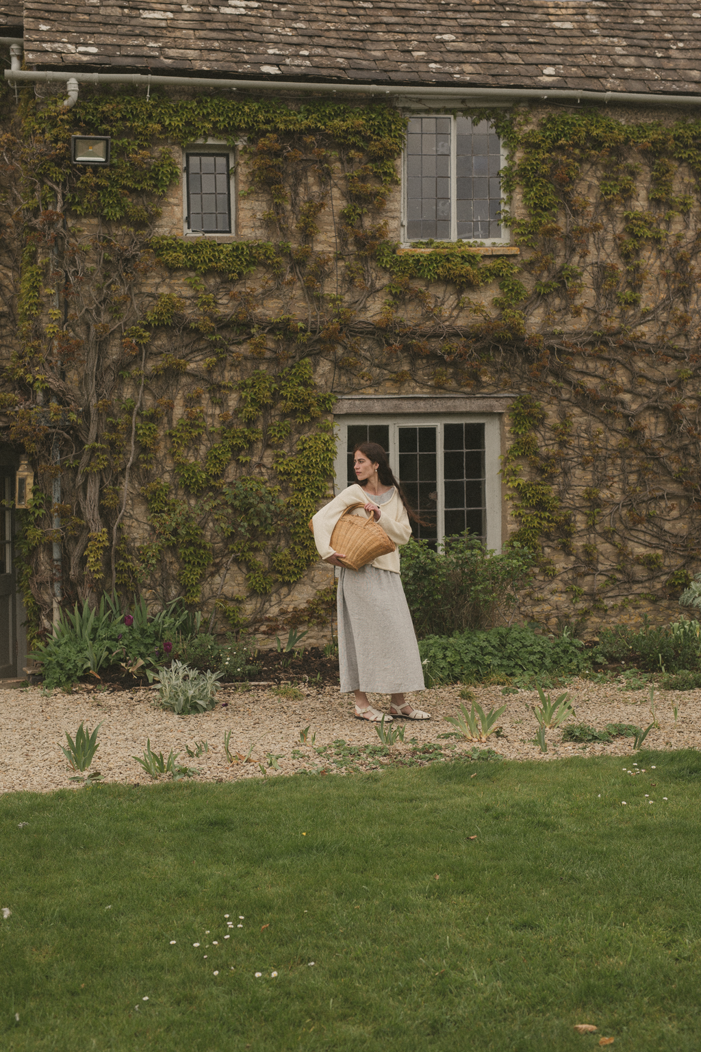 Model wearing the Lennon Cardigan in Ivory by Gillian Stevens, full-length outdoor shot at a stone manor