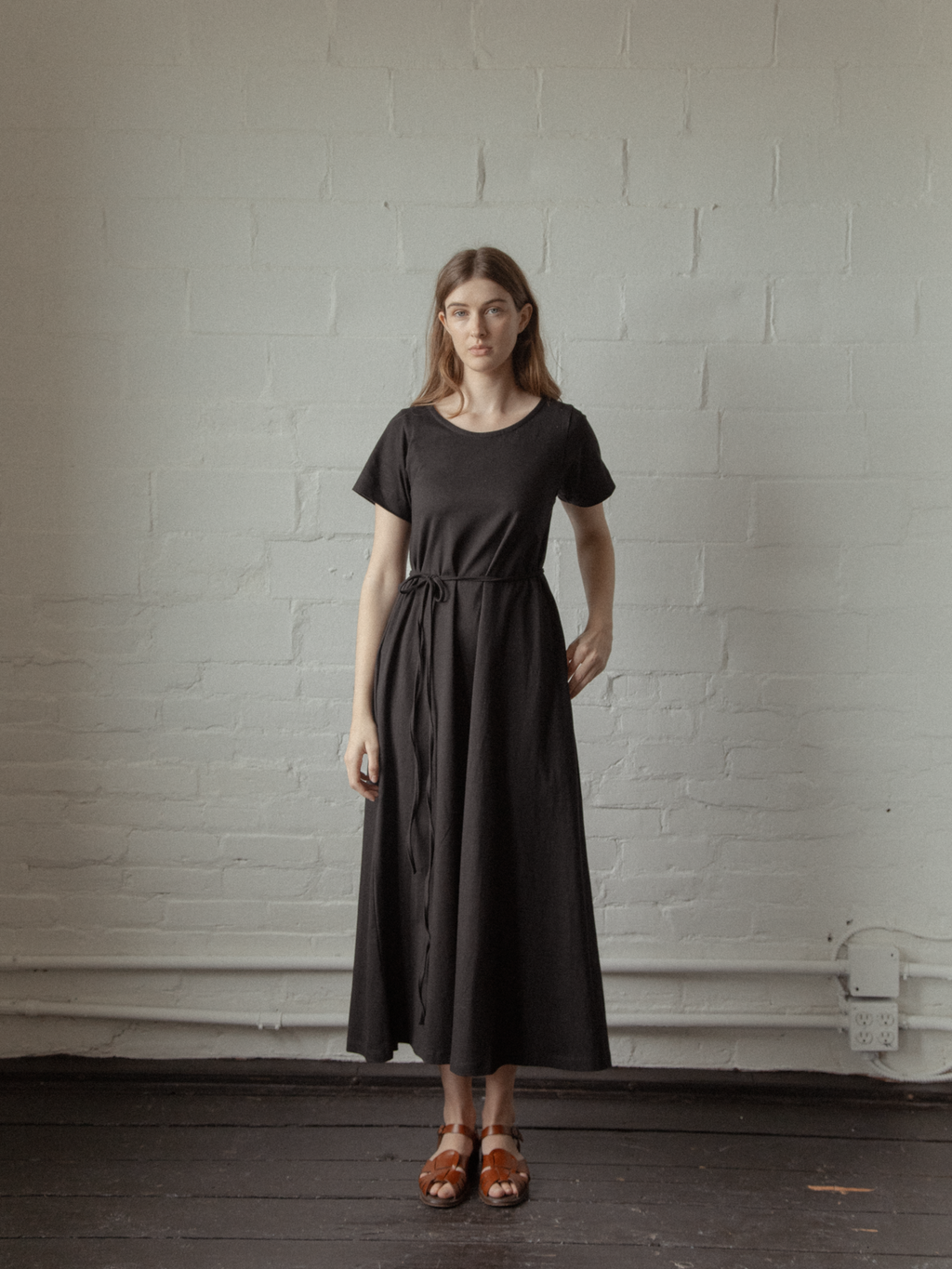 Model wearing the Palmer Dress in Noir by Gillian Stevens, front view showing tie waist and full skirt