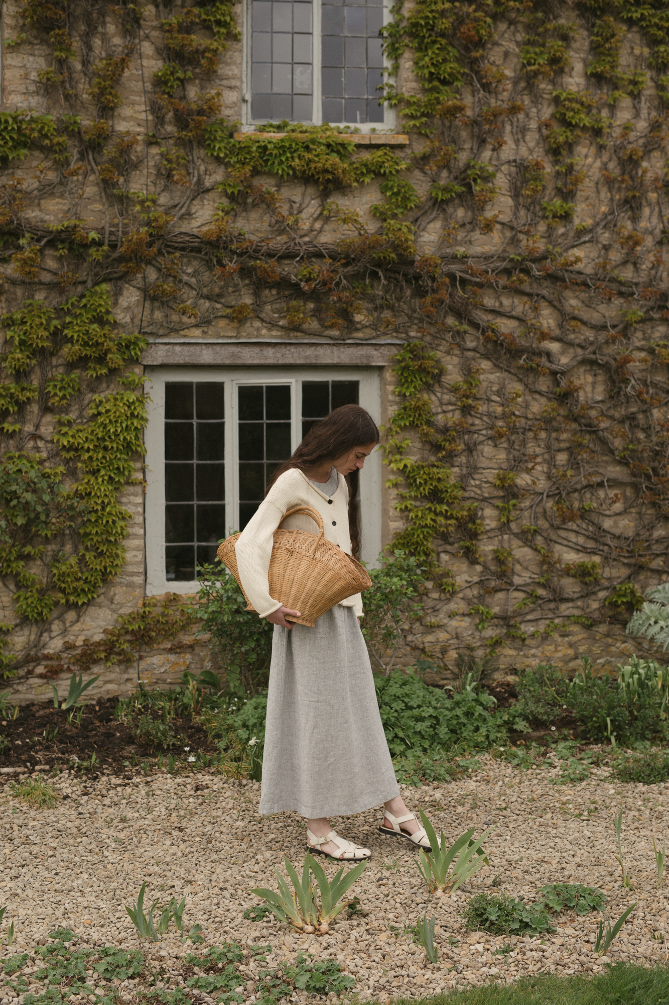 Model wearing the Lennon Cardigan in Ivory by Gillian Stevens, side view in ivy-covered garden setting