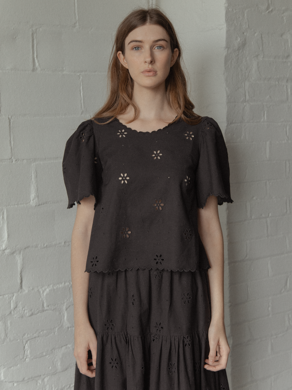 Model wearing the Stella Top in Noir by Gillian Stevens, front view showing broderie anglaise detail and scalloped hem