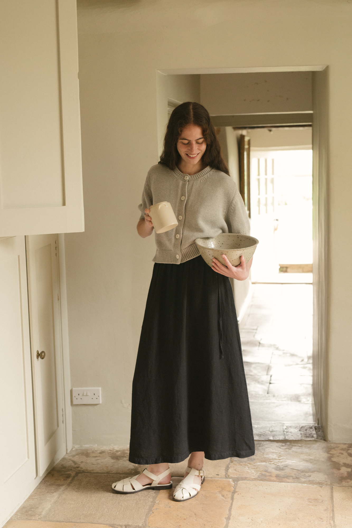 Woman holding a bowl and a  in a home setting wearing the rosemary cardigan in pebble by Gillian Stevens