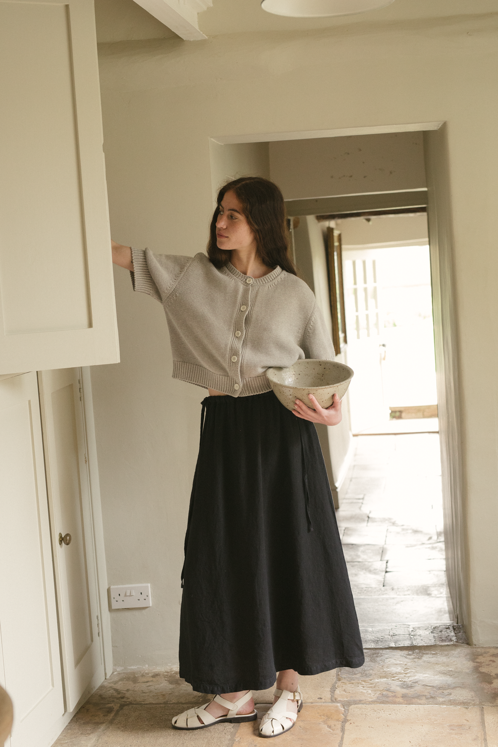 Model wearing the Frances Skirt in Noir by Gillian Stevens, full-length front view in a home setting, view 2