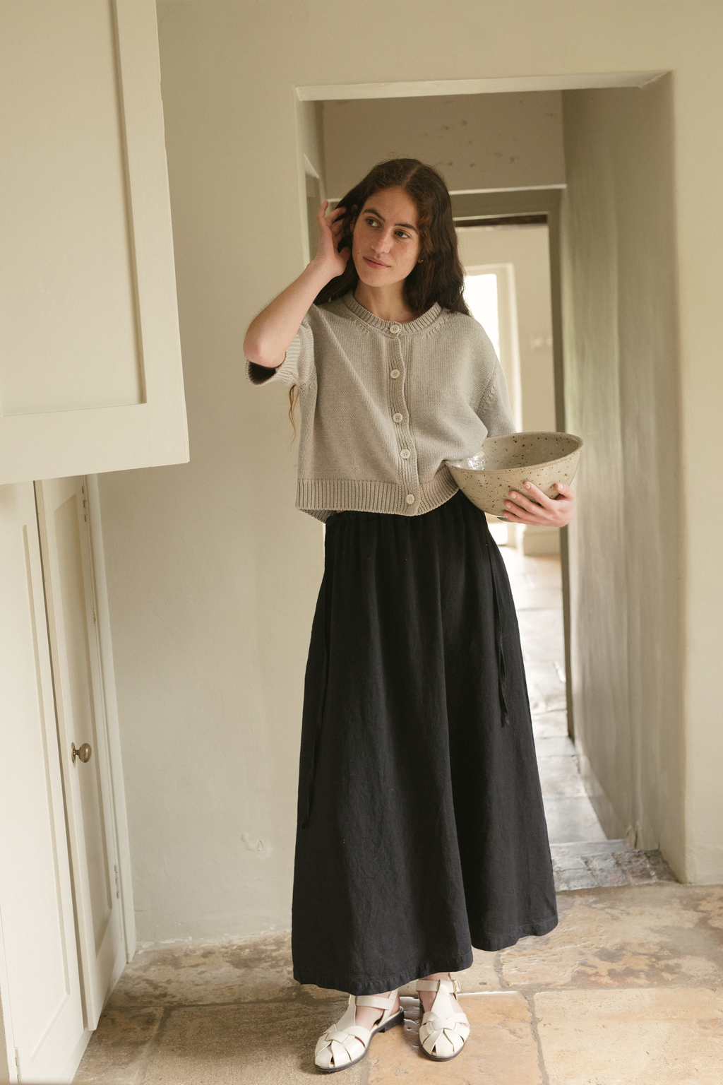 Model wearing the Frances Skirt in Noir by Gillian Stevens, full-length front view in a hallway setting