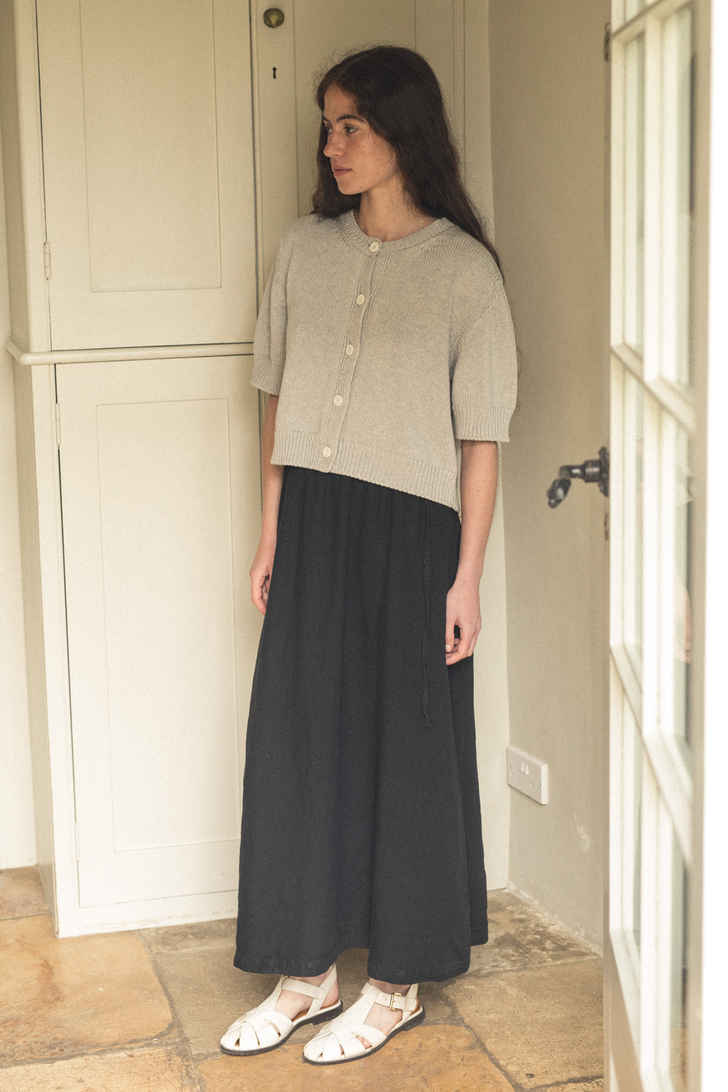 Model wearing the Frances Skirt in Noir by Gillian Stevens, side view styled with a cropped knit cardigan