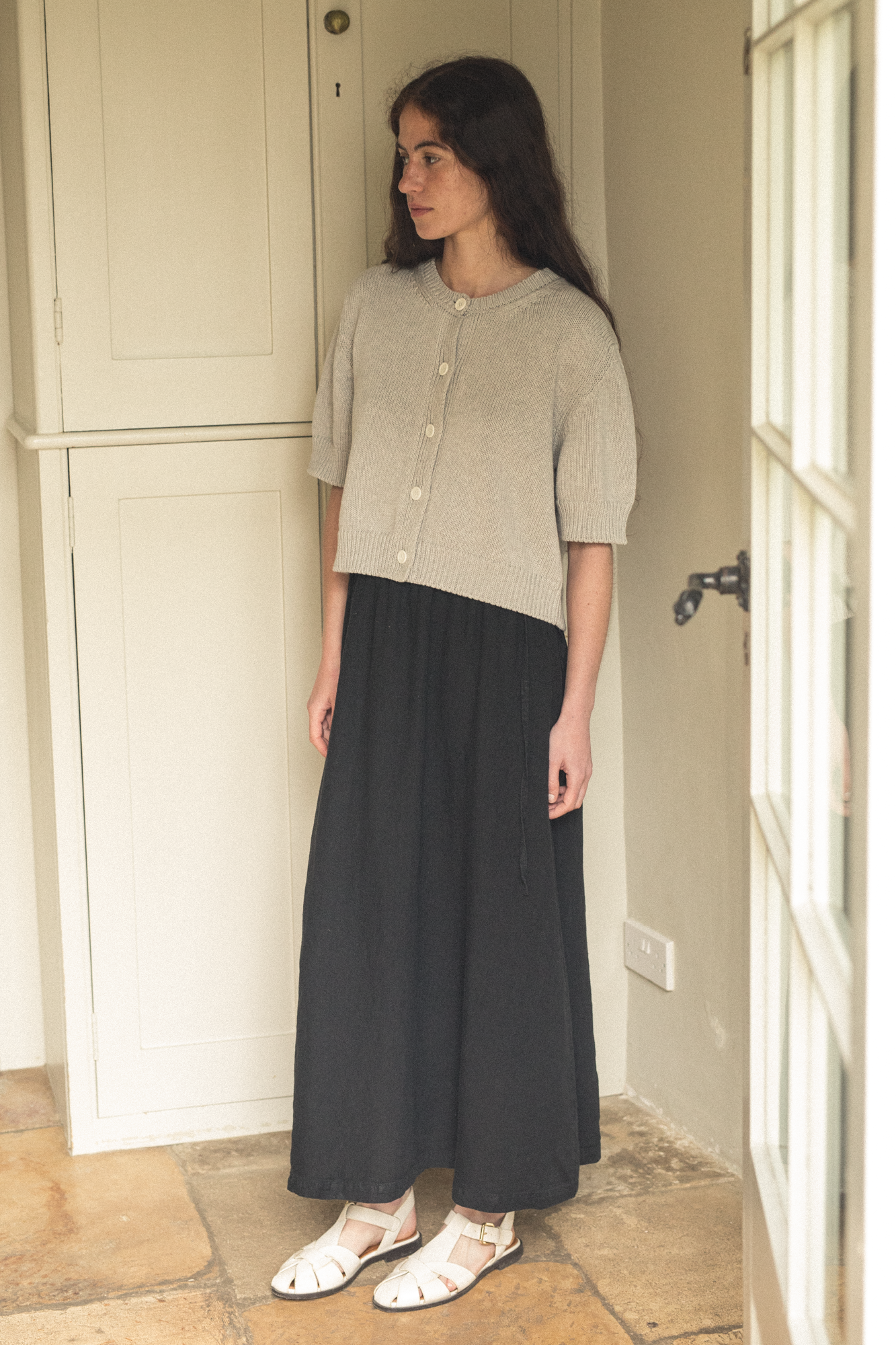 Model wearing the Frances Skirt in Noir by Gillian Stevens, side view styled with a cropped knit cardigan