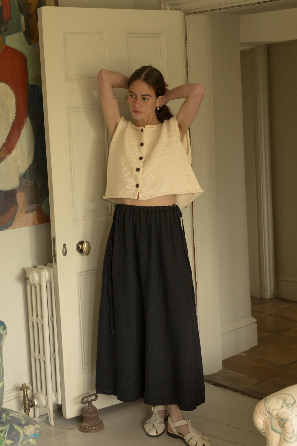 Model wearing the Lennon Vest in Ivory by Gillian Stevens, arms raised in an interior room setting